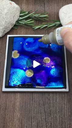 someone is painting something blue and purple on the glass with white paint, next to some rocks