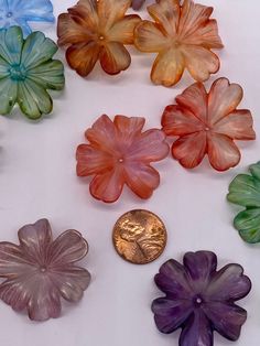 small glass flowers sitting next to a penny on a white surface with one coin in the middle