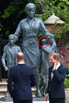 two men in suits standing next to a statue with one man's hand on his head