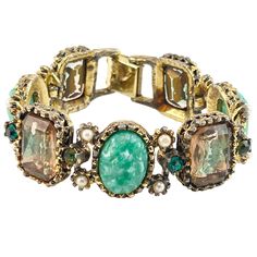 Unsigned Victorian Revival Link Bracelet, adorned with faux pearls and rhinestone green. Made with gold plated metal, this 7" bracelet boasts a unique blend of green, purple, and white color. * Victorian Revival style link bracelet * Features faux pearls and rhinestone green * Made from gold plated metal * Foil backed Rhinestones for added sparkle * Measures 7" in size * Unsigned brand * Blend of green, purple, and white color Features: * Victorian Revival, Link Bracelet, Size: 7" Condition: Pre-Owned Good The foil backing on the back of the rhinestones is worn. It's not perfect but it creates a unique purple gold color. Elegant Green Stretch Bracelet For Party, Green Beaded Metal Bangle Bracelets, Elegant Green Crystal Metal Bracelet, Green Jeweled Bangle Bracelets, Vintage Green Bracelets For Party, Green Costume Jewelry Bracelets For Party, Adjustable Green Crystal Metal Bracelet, Green Metal Bracelet Costume Jewelry, Green Metal Bracelets For Costume Jewelry