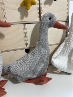 two stuffed ducks sitting next to each other in front of a cabinet with wooden drawers