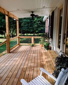 a wooden porch with white rocking chairs and plants on the back deck, looking out to the yard