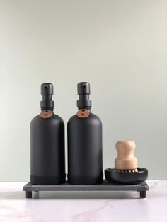 two black bottles sitting on top of a counter next to a brush and soap dispenser