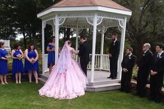 a bride and groom standing in front of a gazebo with their wedding party looking on