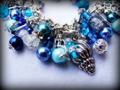 This is a handmade beaded charm bracelet full of wonderful Tibetan silver and silver plated charms, glass beads and pearls inspired by Sirens of the sea. The charms are sea shells, mermaids, turtles, dolphins, starfish and other sea inspired themes with a beautiful dragonfly clasp. This is 7.5 inches long but can be made longer if required :)  In mythology, sirens were seen as beautiful and dangerous creatures depicted as mermaids who used to lure sailors into rocks with their enchanting singing Ocean-inspired Silver Beaded Bracelets, Silver Beaded Ocean-inspired Bracelets, Handmade Silver Beaded Bracelets Ocean-inspired, Ocean-inspired Silver Beaded Jewelry, Silver Beaded Ocean-inspired Jewelry, Handmade Silver Charm Bracelet For Beach, Silver Beaded Bracelet With Lobster Clasp For Beach, Angel Wing Ear Cuff, Dangerous Creatures