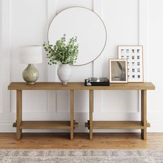 a wooden table topped with a mirror next to a vase filled with green plants and a framed photograph