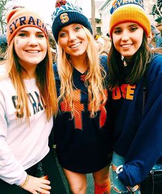 three girls are posing for the camera in front of a group of people wearing beanies and sweaters