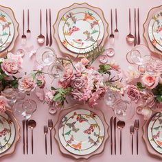 the table is set with pink flowers and gold trimmings, plates and silverware