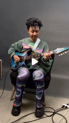 a young man sitting in a chair playing an electric guitar with colorful paint on his leggings