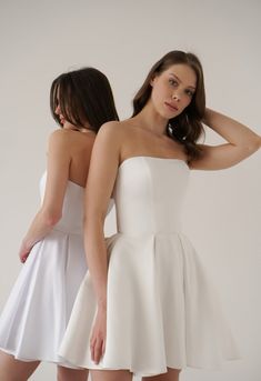 two women in white dresses standing next to each other, one wearing a strapless dress