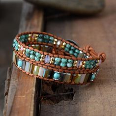 two leather bracelets with beads and glass beads on top of each other, sitting on a piece of wood