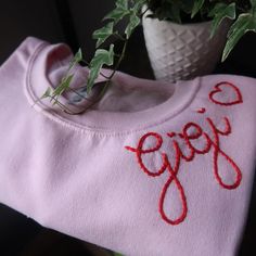 a pink shirt with the word yogo written on it next to a potted plant