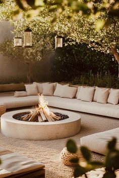 an outdoor fire pit surrounded by pillows and furniture in the middle of a patio area