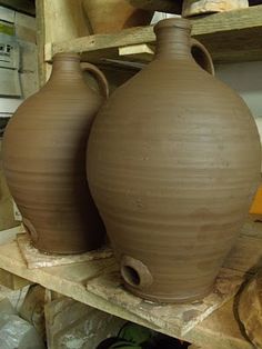 two large vases sitting on top of a wooden shelf in a room filled with pottery