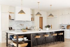 a large kitchen with white cabinets and marble counter tops, gold pendant lights over the island