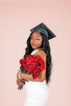 a woman wearing a graduation cap and gown holding roses in her hand while standing against a pink background