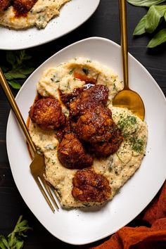 two white plates topped with meatballs and mashed potatoes next to gold utensils