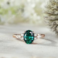 a green and white diamond ring sitting on top of a pine tree branch in front of snow