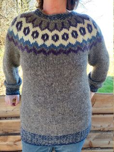 a woman standing in front of a wooden bench wearing a sweater with an intricate design