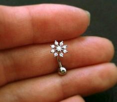 a person is holding a tiny flower shaped nose ring in their left hand and the other end of her finger