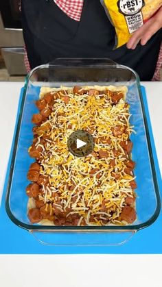 a person holding a bag of chips over a casserole covered in chili and cheese