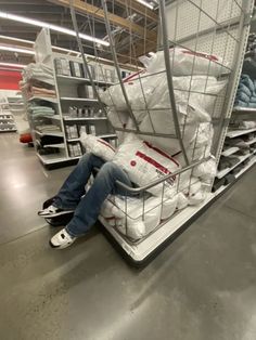 a man is sitting on a shopping cart in a store filled with bags and blankets