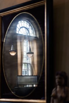 an oval mirror reflecting a room with two lamps hanging from it's ceiling and a statue in the foreground