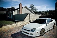 a white sports car parked in front of a brick house on a cobblestone driveway