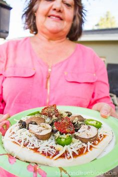 a woman in pink shirt holding a plate with pizza on it and toppings on top