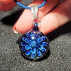 "This is one of my second favorite pendants that I currently have in stock. On a clear base is a beautiful royal blue flower implosion that sparkles from a color called stardust. I make each handmade implosion pendant using a blowtorch and Borosilicate glass in my studio. I love the depth and sometimes, trapped bubbles I can achieve with these pendants. This design reminds me of a lotus blossom trapped in glass. Each of these pendants are one of a kind that I create out of molten glass. I only u Unique Blue Flower Pendant Jewelry, Blue Recycled Glass Jewelry As Gift, Blue Murano Glass Round Jewelry, Blue Recycled Glass Jewelry For Gift, Blue Glass Flower Shaped Jewelry, Blue Flower Shaped Glass Jewelry, Blue Flower-shaped Glass Jewelry, Blue Round Recycled Glass Jewelry, Blue Recycled Glass Round Jewelry