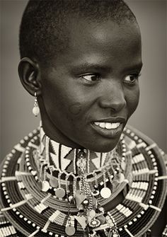 an african woman in traditional dress with necklaces and earrings on her neck, looking at the camera