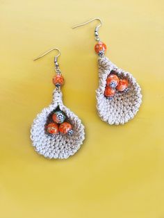 a pair of crocheted earrings with orange beads on them sitting on a yellow surface