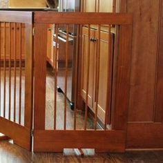 a baby gate in the middle of a kitchen with wood floors and cabinets behind it