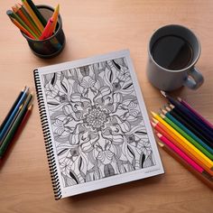 a coloring book, pencils, and cup of coffee sit on a wooden table