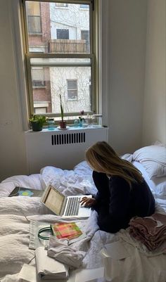 a woman is sitting on her bed with a laptop and papers in front of her