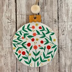 a white ornament with red berries and green leaves hanging on a wooden background