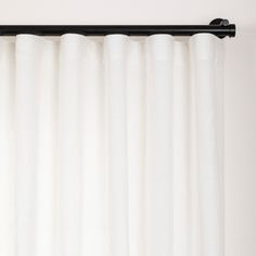 a white curtain hanging on the side of a window with black metal rod ends and an eyelet