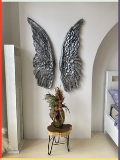 two metal wings hang on the wall above a small table with a potted plant