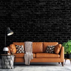 a brown leather couch sitting in front of a black brick wall next to a lamp