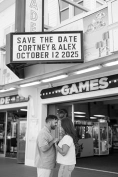 a man and woman standing in front of a building with a sign that says save the date