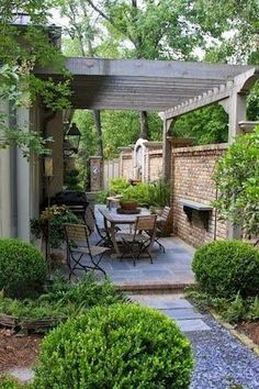 an outdoor dining area with table and chairs in the middle of some bushes, surrounded by trees