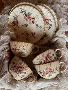 an assortment of porcelain dishes and cups on a lace covered tablecloth with lacy doily