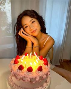 a woman sitting in front of a cake with lit candles