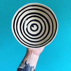 a hand holding up a black and white bowl with an abstract design on it's side