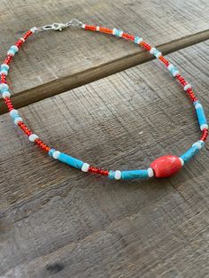 a necklace with red, white and blue beads is on a wooden table next to a bottle