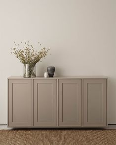 two vases sitting on top of a gray cabinet next to a plant in a vase