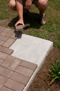 a man kneeling down to put cement on a brick walkway in front of a flower bed