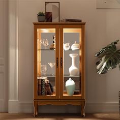 a wooden cabinet with glass doors and vases on the top shelf next to a potted plant