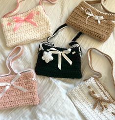 four crocheted purses sitting on top of a white bed next to each other