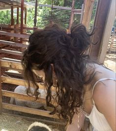 a woman bending down to pet a sheep in a pen with hay on the ground